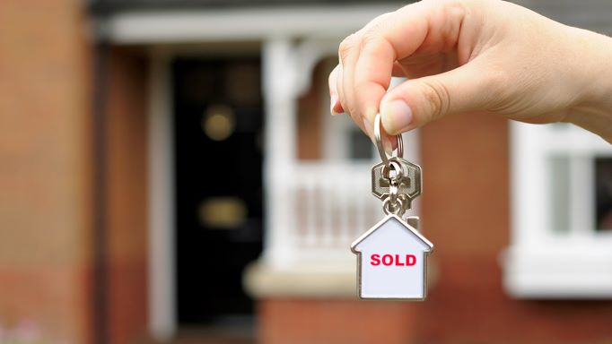 person holding sold keychain in front of house